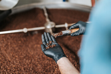 Man's hands holding freshly roasted aromatic coffee beans over a modern coffee roasting machine.