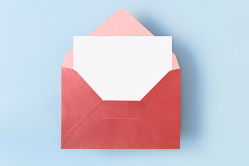 Top view of red envelope with empty blank white card on light blue background, copy space