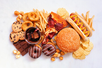 Junk food table scene. Collection scattered over a white marble background. Mixture of take out and...