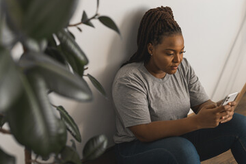 Portrait of African American female student dressed casually holding mobile phone and typing messages and communicating with friends via social networks using high-Internet connection.