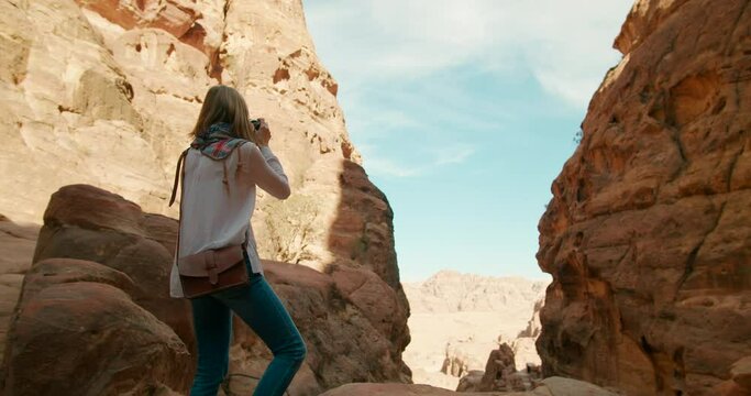 Female tourist visits Petra taking photo of ancient caves carved out of rock cliff. Most popular travel destination in Jordan, Middle East. Woman explore famous world heritage. 4K gimbal orbit shot