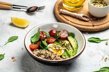 Keto diet plate quinoa, avocado, egg, tomatoes, spinach and sunflower seeds on light background. Healthy food, ketogenic diet, diet lunch concept, place for text, top view