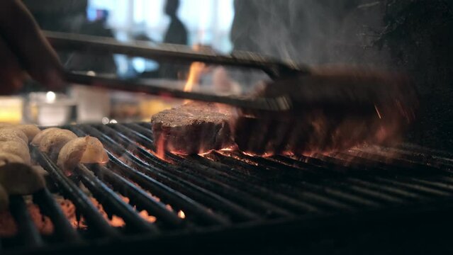 Roasting juicy meat steak with spices and herbs in burning charcoals fire on bbq grid, flames and smoke in slow motion. Juicy steak with grilling stripes ready for picnic celebration. Barbecue grill