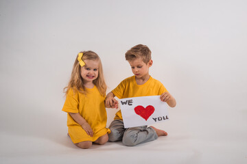 Little happy boy and happy girl with long hair in yellow clothes hold in hands white sheet of paper...