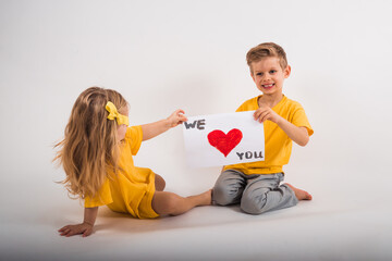 Little happy boy and happy girl with long hair in yellow clothes hold in hands white sheet of paper with words we love you isolated on white background