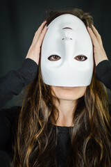 Being different even when wearing a mask - portrait of a young long-haired woman with a mask upside down and hands on her head - concept