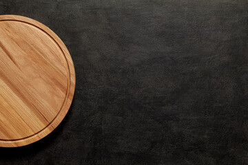 Cutting board round wooden on dark background, top view, space to copy text.