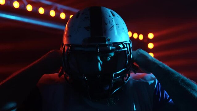 American football championship game: Close up portrait of professional player, removing on helmet. Cinematic slow motion shot against dark background with red blue light.