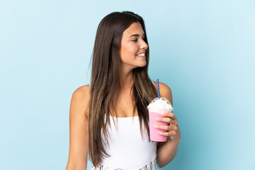 Young brazilian woman with strawberry milkshake isolated on blue background looking to the side and smiling