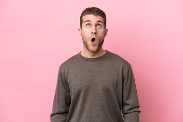 Young caucasian man isolated on pink background looking up and with surprised expression