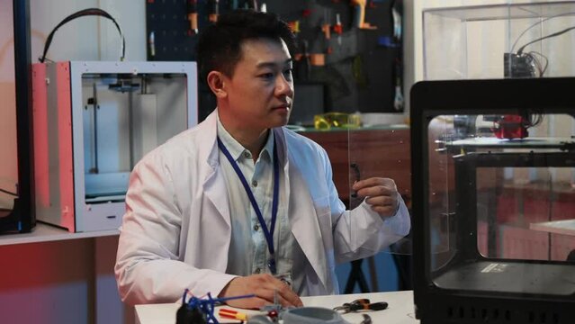 Portrait of asian chinese young developer scientist wearing lab coat working with three dimensional engineering printer technology.