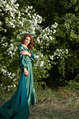 A model in a green silk floor-length dress in a blooming apple orchard. Spring.