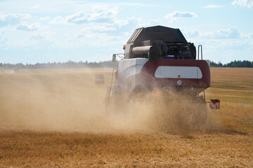 Grain plantation.  A grain harvester threshes wheat ears. A trail of dust follows him. Selective...