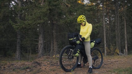 The woman travel on mixed terrain cycle touring with bike bikepacking outdoor. The traveler journey with bicycle bags. Stylish bikepacking, bike, sportswear in green black colors. Magic forest park.