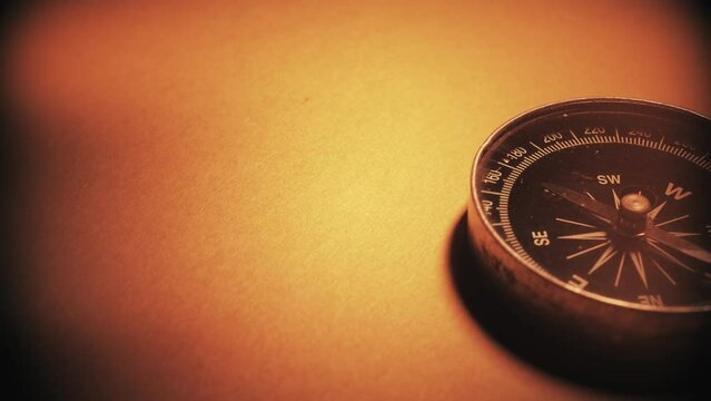 Macro close-up shot of antique compass rotating on old parchment paper texture. Shot on 4K DSLR..