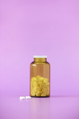 White pills, medical tablets, placebo or vitamins and brown bottle with medicine on purple background closed up, vertical plane, centered