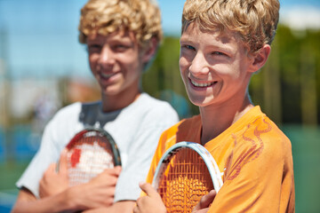 Tennis is their sport of choice. Two friends standing together and holding their tennis rackets on...