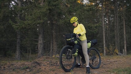 The woman travel on mixed terrain cycle touring with bike bikepacking outdoor. The traveler journey with bicycle bags. Stylish bikepacking, bike, sportswear in green black colors. Magic forest park.