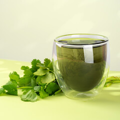 Glass of liquid chlorophyll and fresh herbs on a green table. Concept of superfood, healthy eating, detox and diet. Light green background, square. Close up