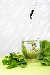 Mixing water and liquid chlorophyll with dropper. Fresh herbs and green towel on a table. Concept...