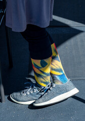 funky street style woman's feet and legs with colorful patterned socks and grey tennis shoes in shadows
