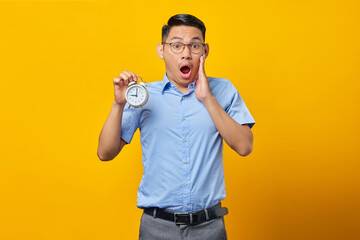 Shocked young Asian woman in glasses holding document folder with open mouth isolated on yellow background. Time management lifestyle concept