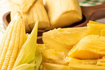 Brazilian corn snack pamonha and cornflower arranged on a table with green and white tablecloth, selective focus.