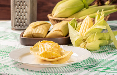 Brazilian corn snack pamonha and cornflower arranged on a table with green and white tablecloth, selective focus.