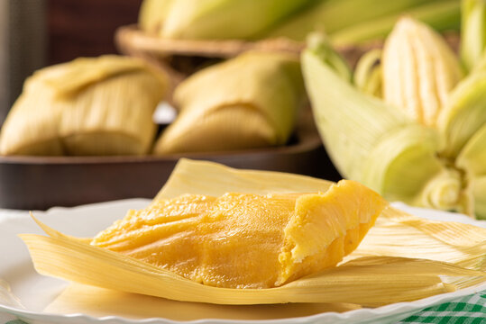 Brazilian corn snack pamonha and cornflower arranged on a table with green and white tablecloth, selective focus.
