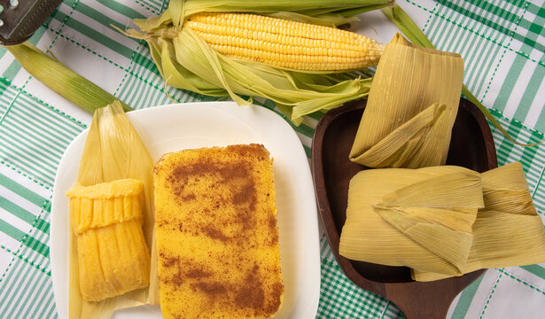 Brazilian Cural, candy corn and pamonha, corn on the cob arranged on a table with a green and white tablecloth, dark background, Top view.