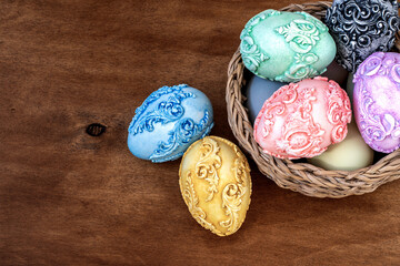 Six carved vintage easter eggs in a wicker basket with a dark wooden background. Easter background with unusual easter eggs. Top view.