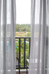 A window with a transparent tulle, access to a balcony overlooking palm trees in a tropical country. Travel and tourism