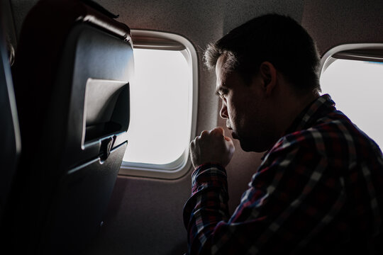 a man in a plaid shirt coughs on the plane in a window seat. 