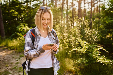 Young woman using mobile phone while walking in the woods during summer hike