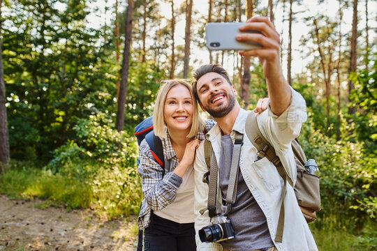 Young couple taking selfie picture with smartphone while hiking in the woods