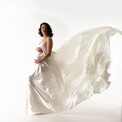 Happy woman waiting for a baby, wrapped in flowing white silk on a white background. The concept of...