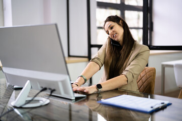 Young Businesswoman On Call While Using Computer At Desk