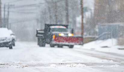 Snow storm plow, small USA town road covered in snow, during snow storm, cars traffic, bad weather travel.
