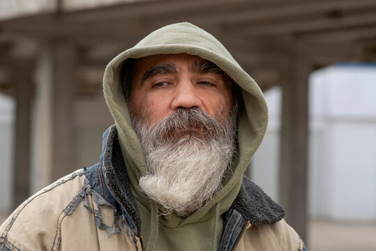 Portrait of an Senior elder man in a hoodie with a gray beard in a shabby clothes outdoors in city