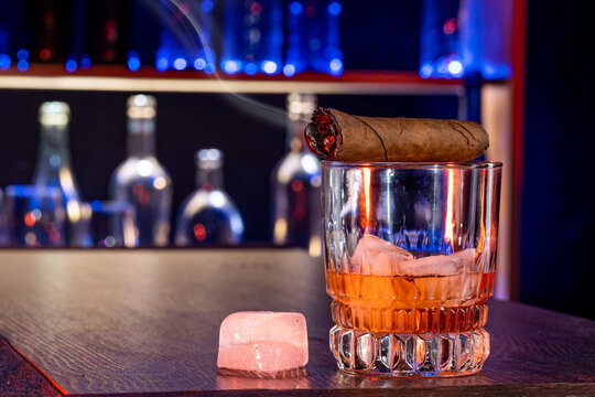 Cigar, elegant glass of brandy on the bar counter. Alcoholic drinks, cognac, whiskey, port, brandy, rum, scotch, bourbon. Vintage wooden table in a pub at night