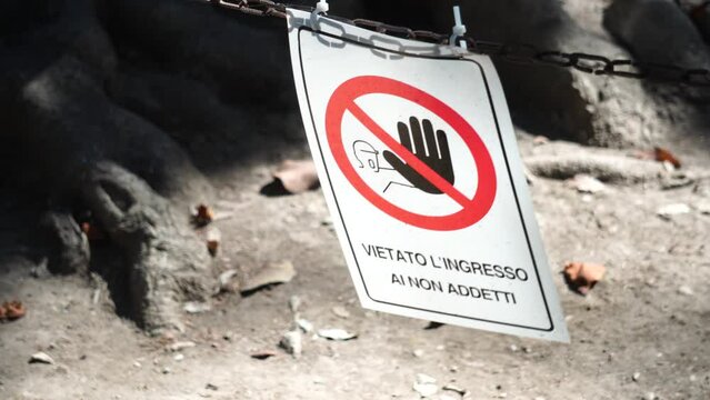 sign with the inscription in Italian: NO ACCESS TO NON-EMPLOYEES FORBIDDEN, on a chain moved by the wind, with a stylized descriptive image, in the morning sun