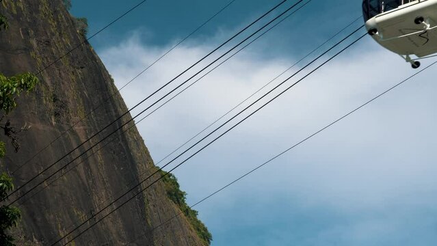 P&atilde;o de A&ccedil;ucar cable car passing with the hill in the background. Neighborhood of Urca, in Rio de Janeiro, Brazil. Sunny day with some clouds at dawn.