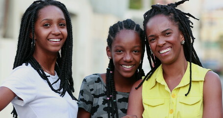 Casual black African mother and teenage daughters standing outside smiling and laughing