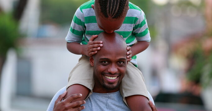 African father and son bonding. Kid kissing dad bald head, child on top of father shoulders