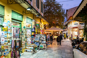 A narrow street of gift and souvenir shops and cafes in the colorful illuminated Plaka district at night in Athens, Greece.