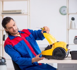 Young male contractor repairing vacuum cleaner at workshop