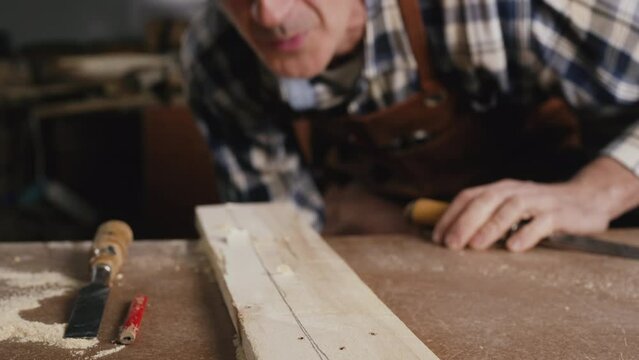 Carpenter blowing sawdust away from handcrafted wood plank on workbench. Artisan worki . Build home creative ideas. High quality 4k footage