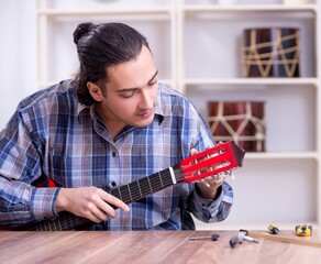 Young handsome repairman repairing guitar