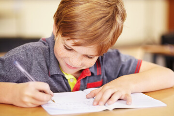 Naklejka premium Happy to do his homework. A cute little boy doing his homework in class.