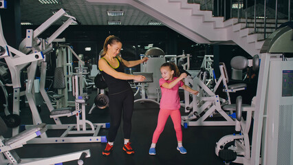 Mother and Daughter in the Gym, Family Performs Physical doing Exercises Fitness, Healthy Lifestyle. Happy Sports Family Training Concept. Woman with her Child doing Stretching Warm-up in the Gym